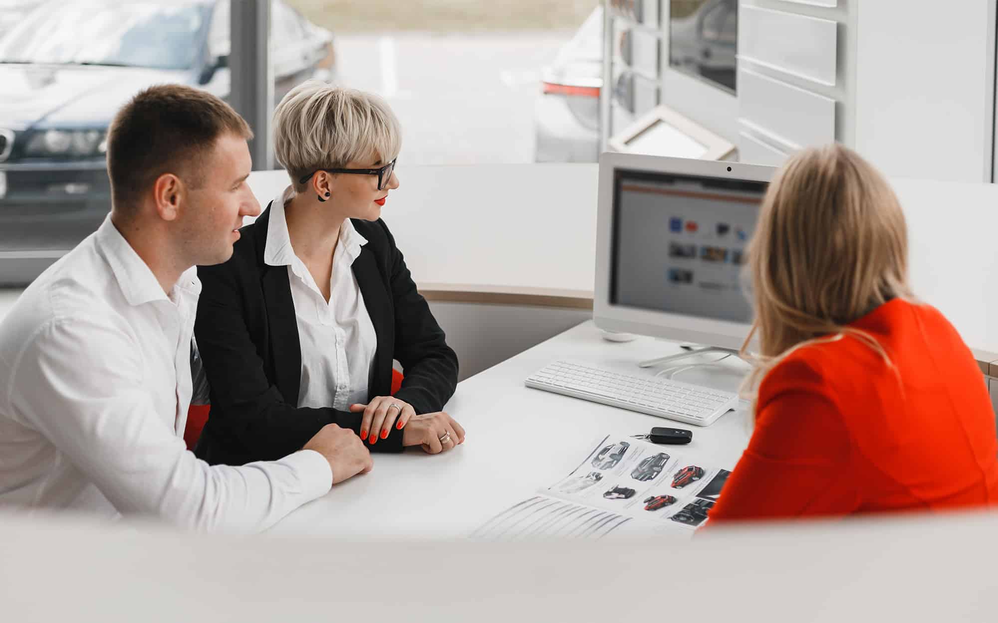 Back view of multiple people looking at computer at car dealership