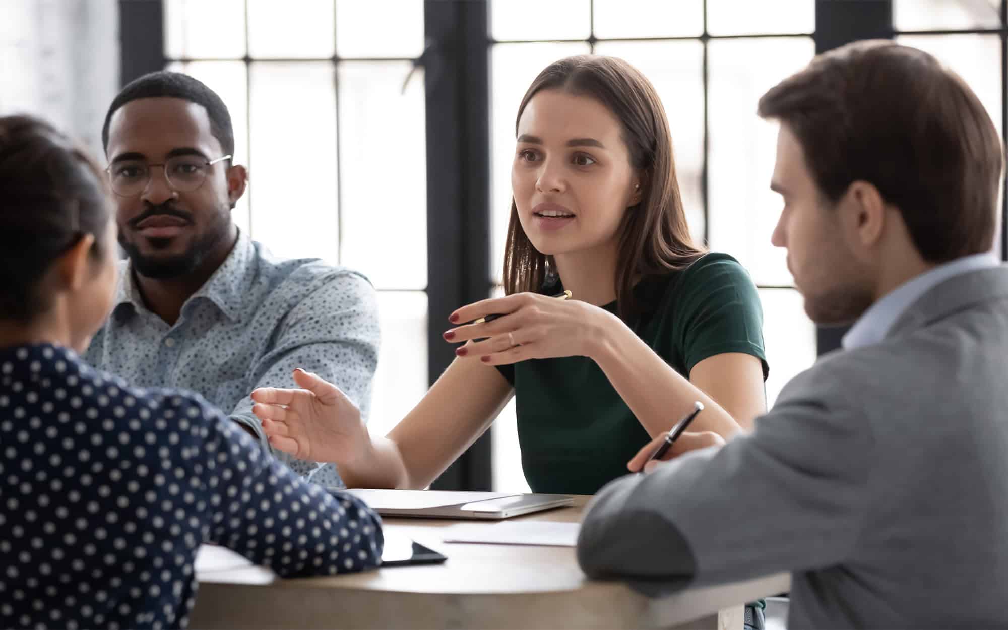 Team meeting, woman talking to her team while sitting at a table