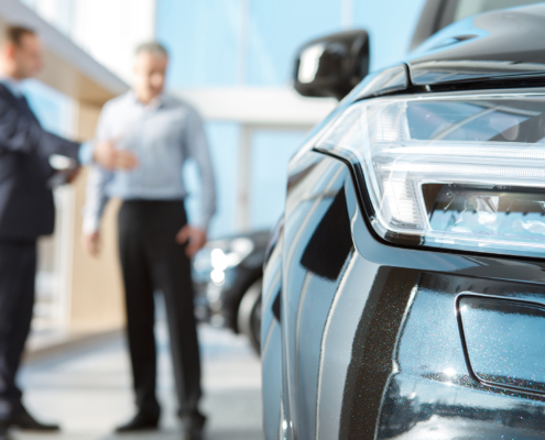 Professional salesman and his male customer at the car dealership showroom