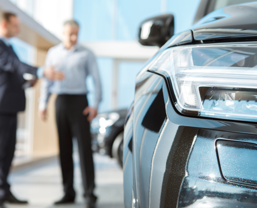 Professional salesman and his male customer at the car dealership showroom