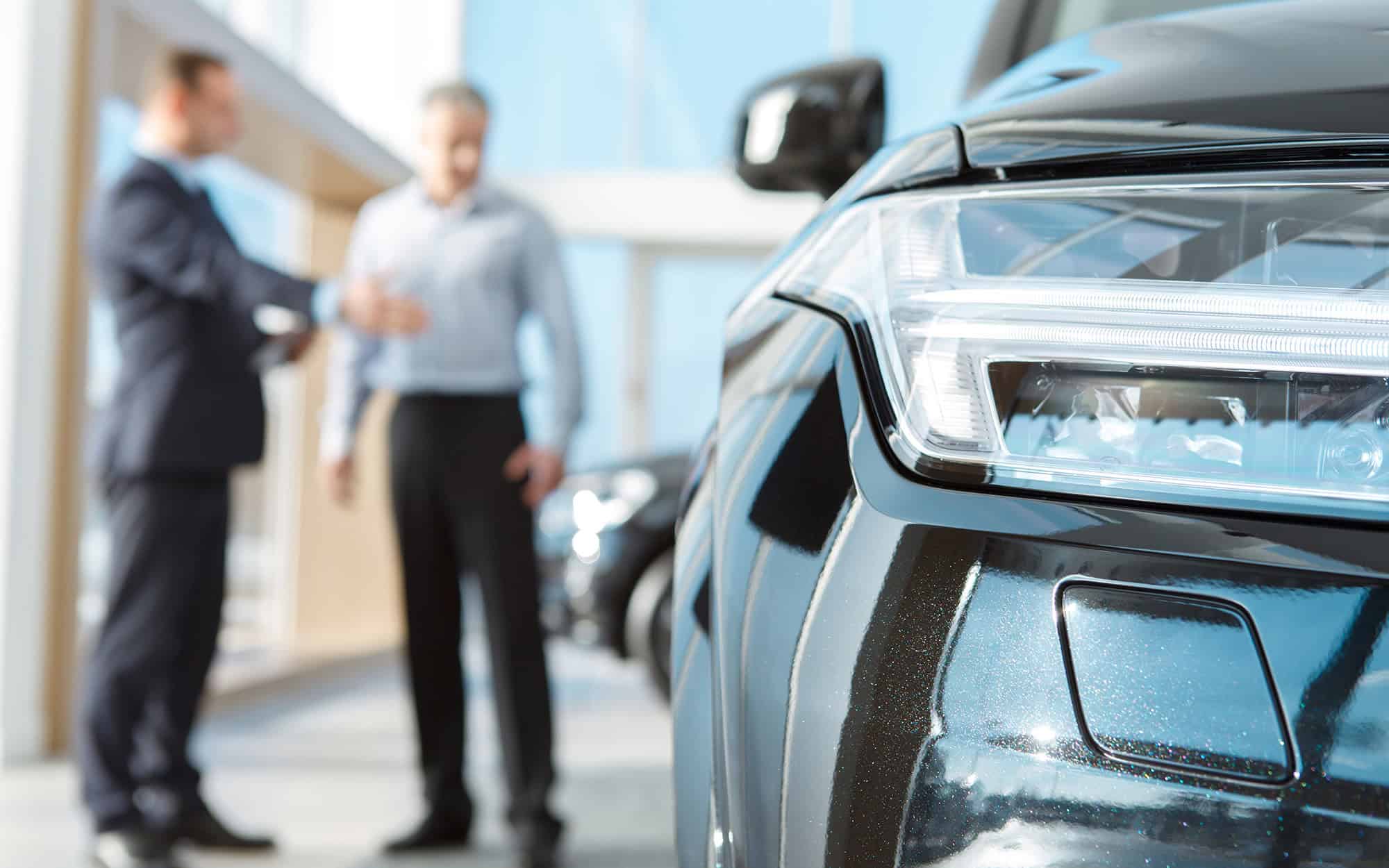 Professional salesman and his male customer at the car dealership showroom Professional salesman and his male customer at the car dealership showroom
