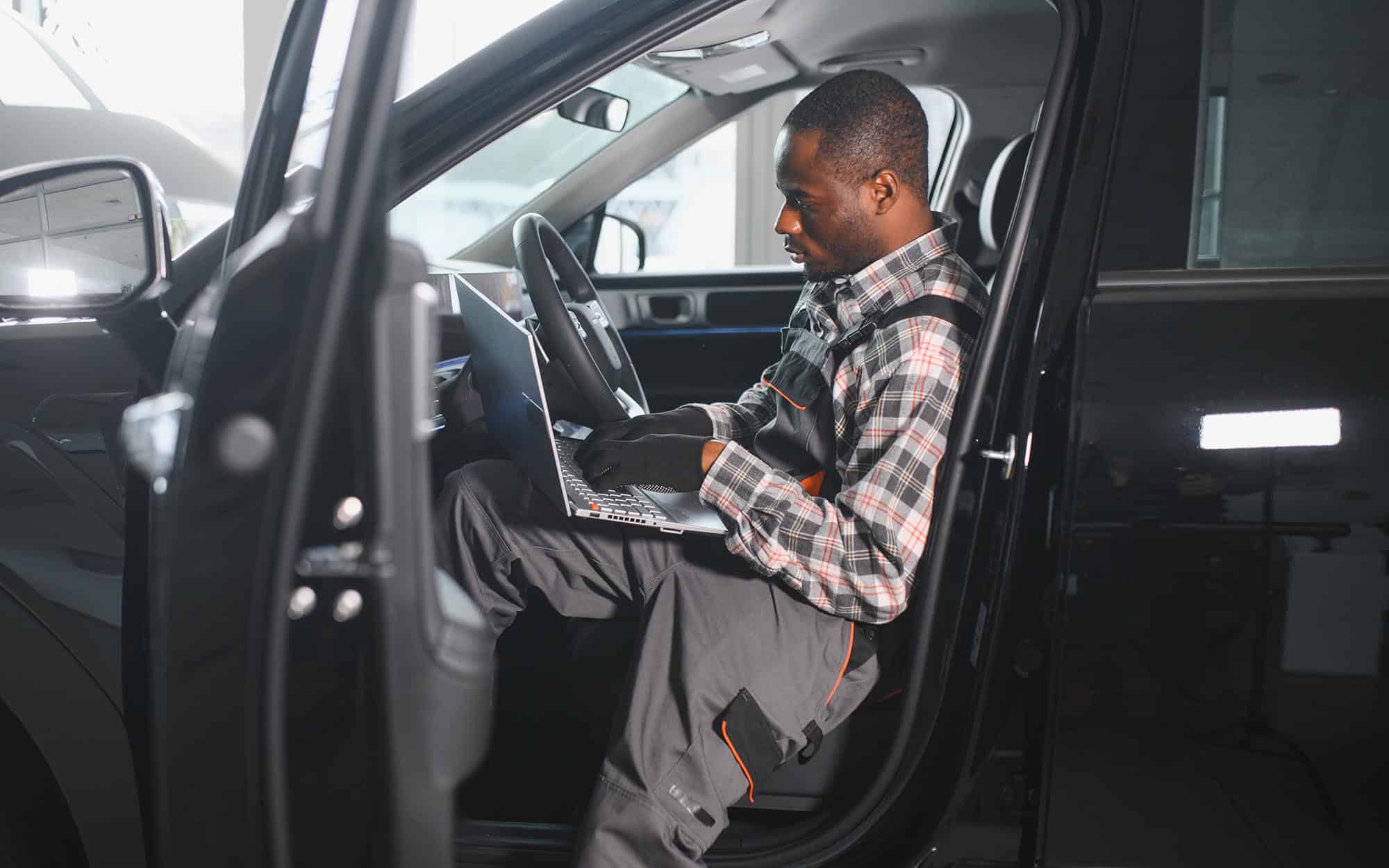 Car technician looking at information on laptop while working on car