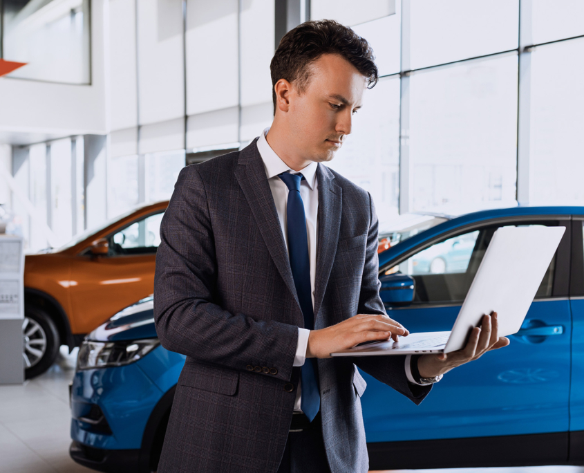 An employee of a dealership in a suit stands against the background of cars An employee of a dealership in a suit stands against the background of cars